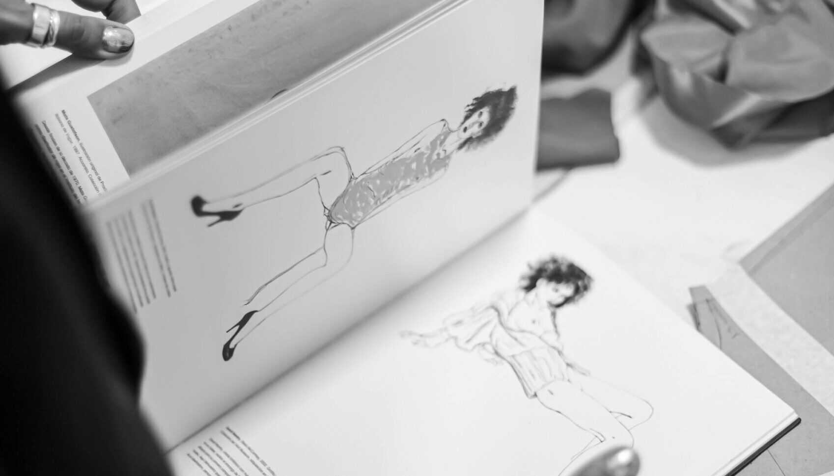 A fashion designer flips through a sketchbook filled with croquis in a creative studio setting.